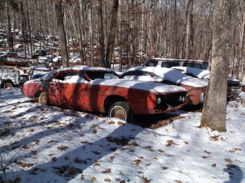 1974 Dodge Challenger - A 1974 Dodge Challenger sits in a snowy junkyard, its red and white paint faded and weathered.
