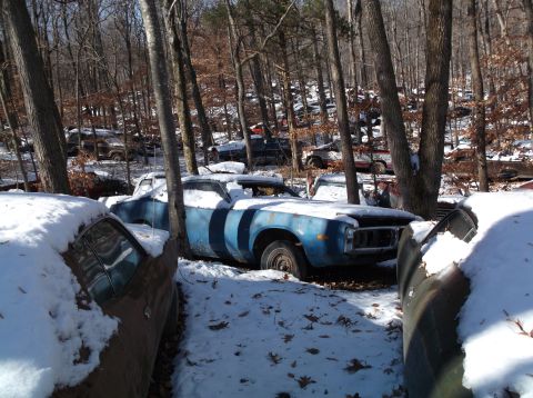 1974 Dodge Challenger - A weathered car sits in a snowy junkyard, surrounded by trees and other vehicles.