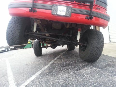 1995 Ford Bronco - The rear axle and suspension of a red SUV are visible, with a '4x4' badge on the body.