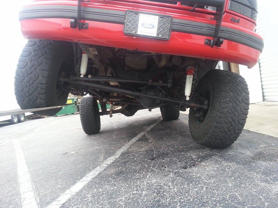 Rear underside of a red SUV, showing the axle, suspension, and large tires. A '4x4' badge is visible