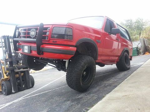 1995 Ford Bronco - A red 1995 Ford Bronco is being lifted by a forklift, its lifted suspension and off-road tires.