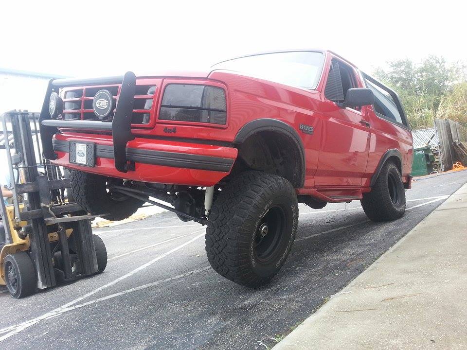 Red 1995 Ford Bronco lifted by a forklift, front 3/4 view