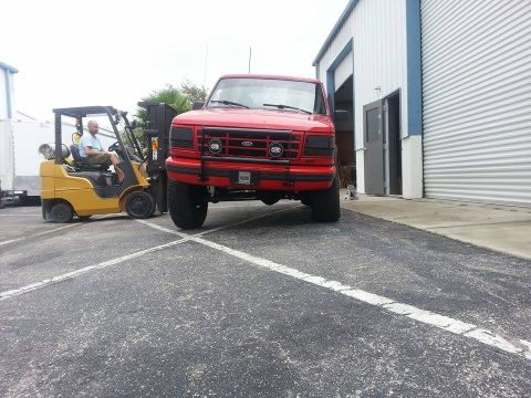 1995 Ford Bronco - A red 1995 Ford Bronco is parked in front of a warehouse, with a forklift operator nearby.