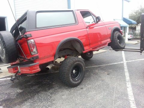 1995 Ford Bronco - A red 1995 Ford Bronco is being lifted by a forklift, with its spare tire visible on the rear.