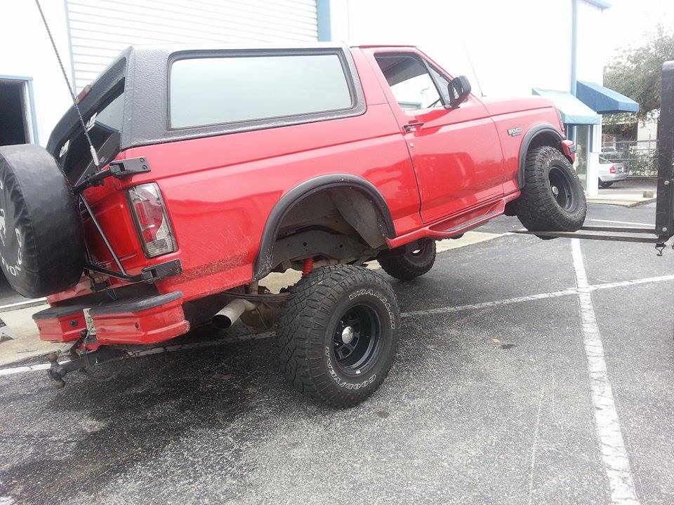 Red 1995 Ford Bronco lifted by a forklift, spare tire mounted on rear door