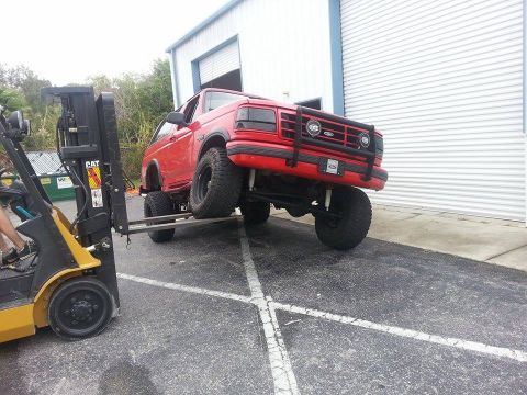1995 Ford Bronco - A red 1995 Ford Bronco, modified with a lifted suspension, is being repositioned using a forklift.