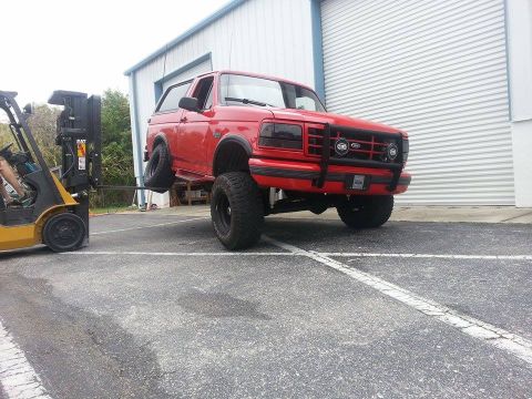 1995 Ford Bronco - A red 1995 Ford Bronco is being lifted by a forklift in front of a large garage door.