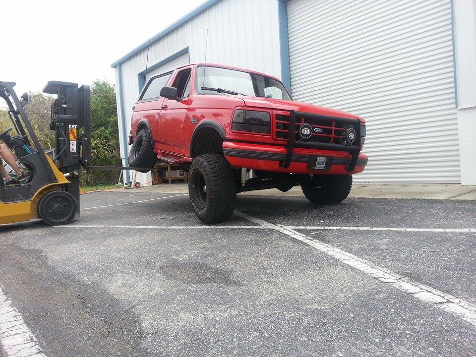 Red 1995 Ford Bronco lifted by forklift