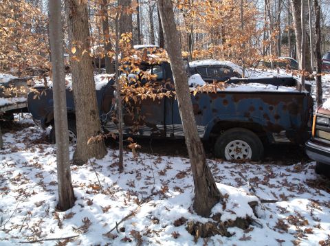 1974 Dodge Challenger - Abandoned blue pickup truck sits in a snowy forest with other vehicles nearby.