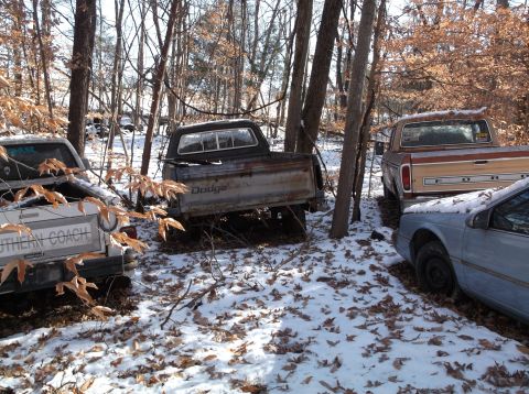 1974 Dodge Challenger - A collection of vehicles sits abandoned in a snowy, wooded area, with one truck clearly marked as 'Dodge'.