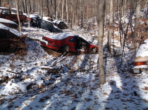 1974 Dodge Challenger - A junkyard scene with multiple vehicles covered in snow amongst trees.