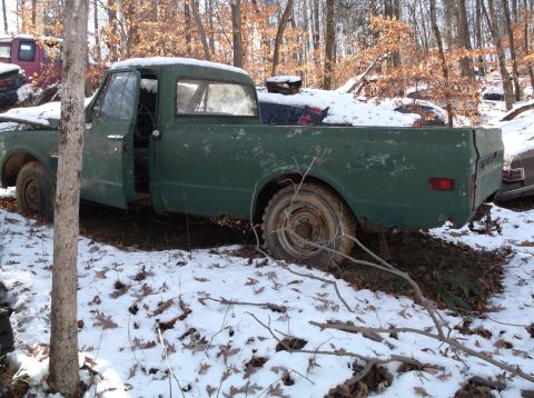 1974 Dodge Challenger - A green pickup truck sits in a snowy wooded area, with another vehicle partially visible in the background.