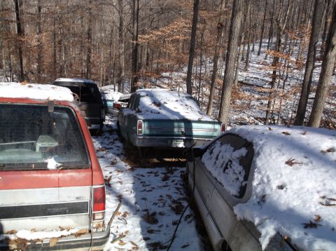 1974 Dodge Challenger - Multiple vehicles sit abandoned in a snowy forest, with a teal sedan partially visible.