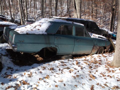 1974 Dodge Challenger - An abandoned aqua sedan sits in a snowy junkyard, missing its wheels and showing signs of rust.