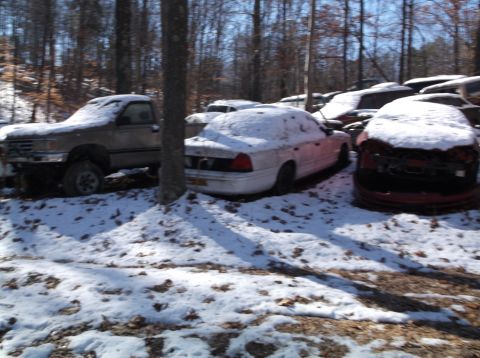 1974 Dodge Challenger - A collection of vehicles sits covered in snow in a junkyard setting.