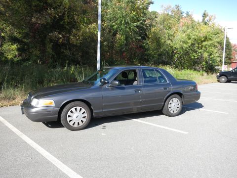 2001 Ford Crown Victoria - A dark grey sedan is parked in a lot with trees in the background.