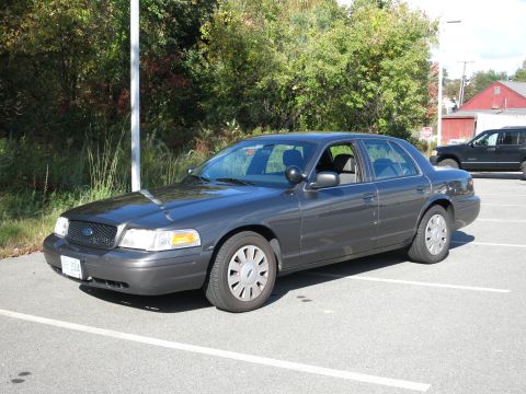2001 Ford Crown Victoria - Dark grey 2001 Ford Crown Victoria parked in a lot with trees and a building in the background.