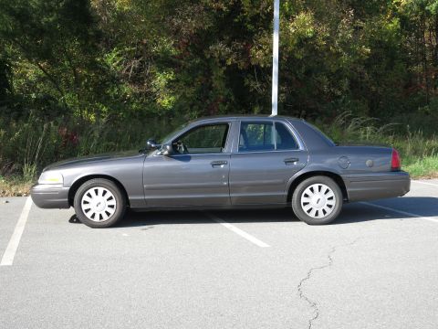 2001 Ford Crown Victoria - A gray 2001 Ford Crown Victoria is parked in a lot with trees in the background.