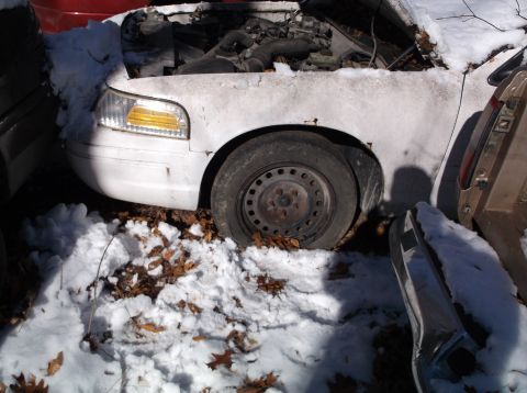1974 Dodge Challenger - A white sedan sits in the snow with its hood open, partially obscured by other vehicles.