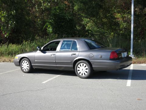 2001 Ford Crown Victoria - A grey sedan is parked in a lot with trees in the background.
