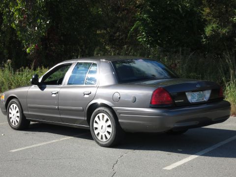 2001 Ford Crown Victoria - A gray 2001 Ford Crown Victoria is parked in an outdoor lot with trees in the background.