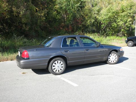 2001 Ford Crown Victoria - A dark grey sedan is parked in a lot on a sunny day, with trees and another vehicle visible.