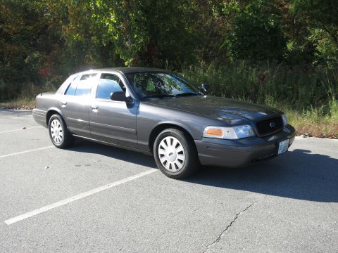 2001 Ford Crown Victoria - A 2001 Ford Crown Victoria is parked in a lot with trees in the background.