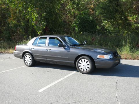 2001 Ford Crown Victoria - A grey 2001 Ford Crown Victoria is parked in a lot with trees in the background.