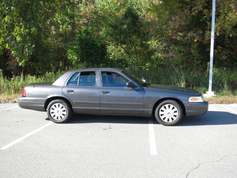 2001 Ford Crown Victoria - A gray 2001 Ford Crown Victoria is parked in a lot with trees in the background.