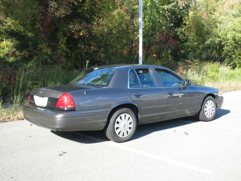 2001 Ford Crown Victoria - A dark grey 2001 Ford Crown Victoria sedan is parked in a lot, viewed from the rear three-quarter angle.