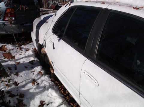 1974 Dodge Challenger - A white sedan sits in the snow, partially obscured by a dark vehicle and fallen leaves.