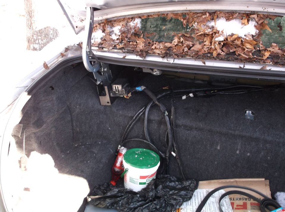 Car trunk interior with leaves and snow on the rear window ledge, wires, and a bucket