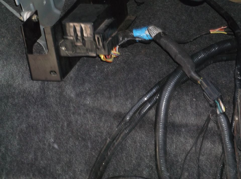 Automotive wiring harness and junction box with blue tape and connectors on gray carpet