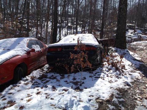 1974 Dodge Challenger - Two cars sit abandoned in a snowy junkyard, with the rear of a black Dodge GT visible.
