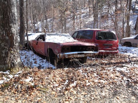 1974 Dodge Challenger - An old, weathered muscle car sits abandoned in a snowy wooded area next to a red minivan.