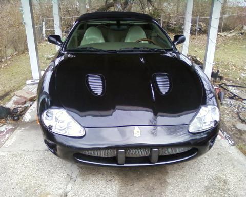 1998 Ford Crown Victoria - A black Jaguar XK8 convertible is parked under a carport, showing its front grille and headlights.