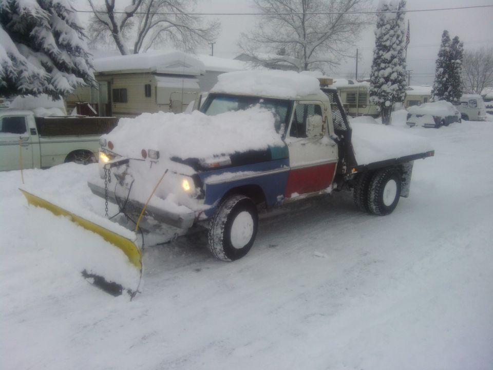 Ford F-series truck with snow plow covered in snow.
