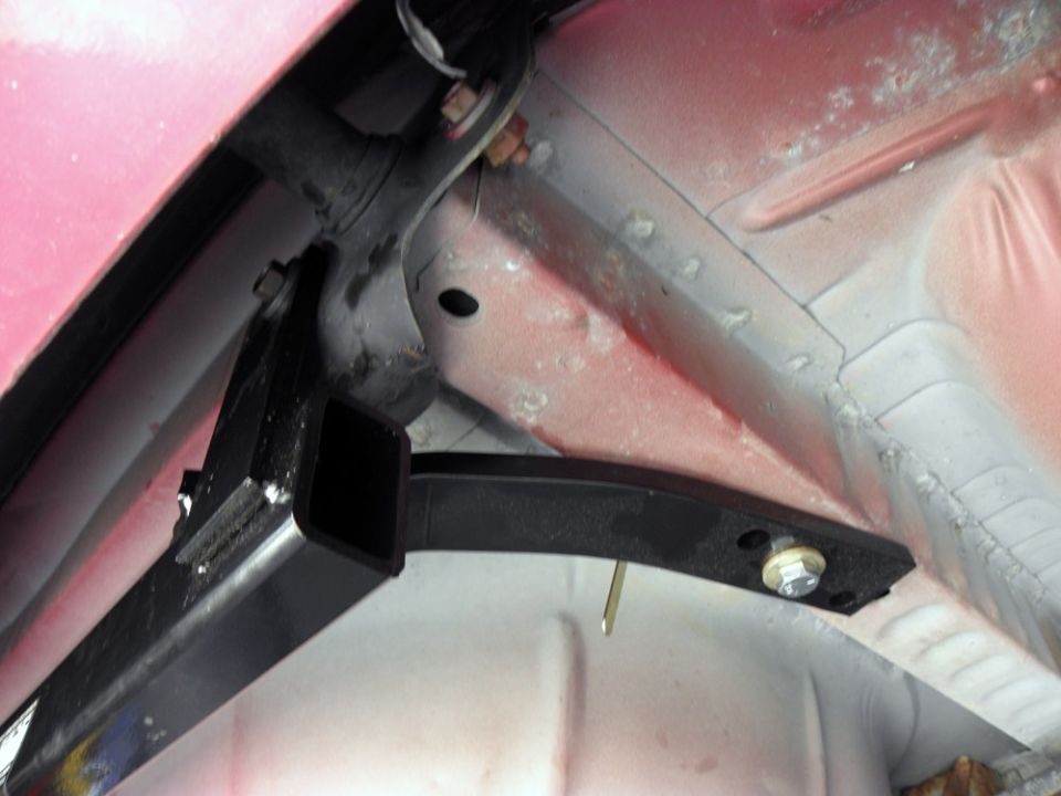 Underside view of a red vehicle with a black trailer hitch receiver installed.