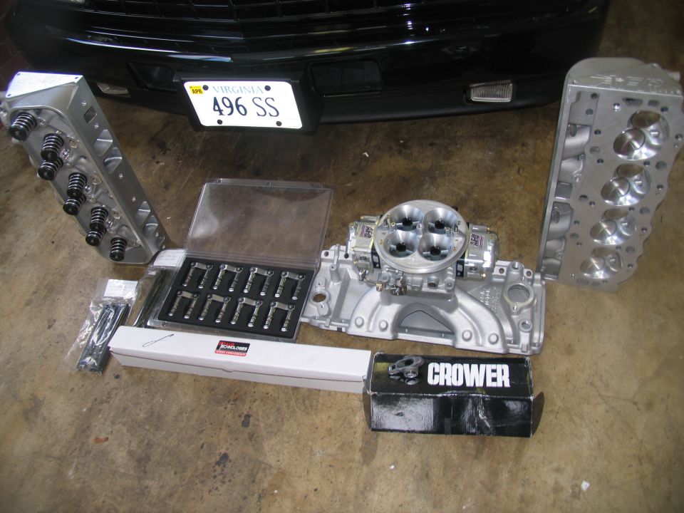 Engine parts including cylinder heads, intake manifold, carburetor, and valve components on a concrete floor.