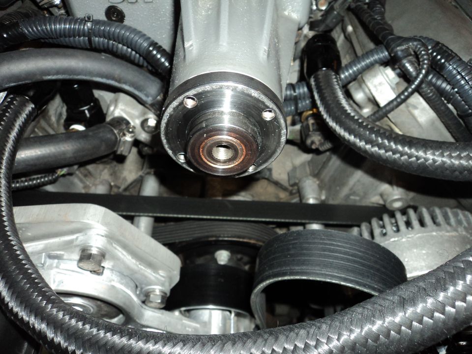 Close-up of car engine showing supercharger, serpentine belt, and hoses.