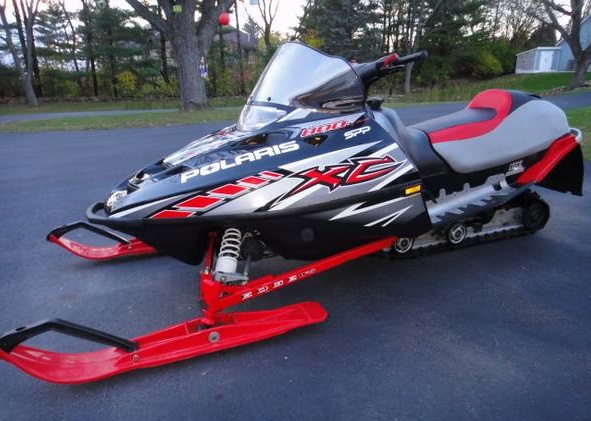 Black and silver Polaris 800 XC SP snowmobile with red accents, parked outdoors.