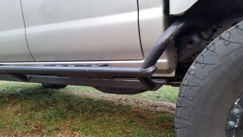 Silver pickup truck with black rock slider and tire.