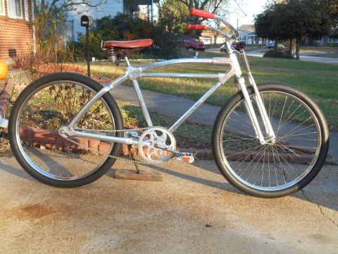 Vintage silver bicycle with red saddle and handlebars, parked on a driveway.