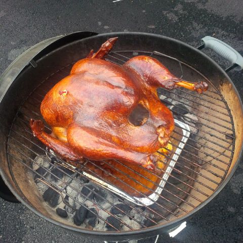 1978 Ford Bronco - A whole roasted turkey is on a grill over hot coals, placed in a foil pan.