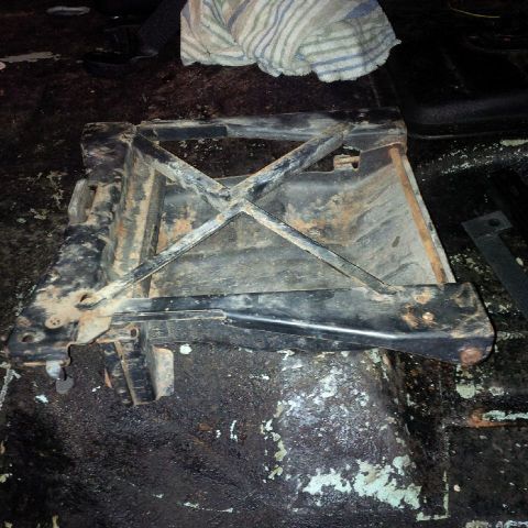 1978 Ford Bronco - A rusty black metal seat frame with an X-shaped support structure is shown resting on a dark, wet, and dirty floor. The frame appears to be…