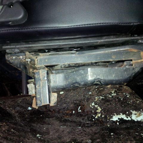 1978 Ford Bronco - This is a close-up view of the rusted metal seat mounting hardware and the underside of a black leather seat in a vehicle. The seat mechani…