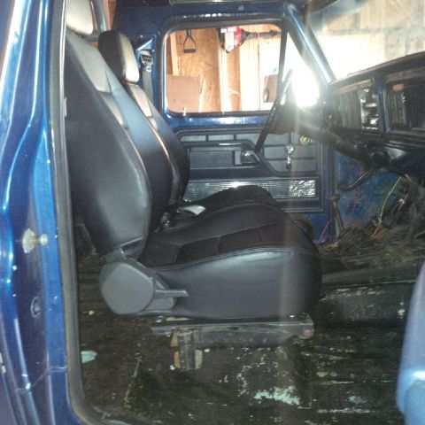1978 Ford Bronco - The interior of a blue Ford truck is shown, featuring black bucket seats and exposed floorboards. The dashboard and steering wheel are visi…