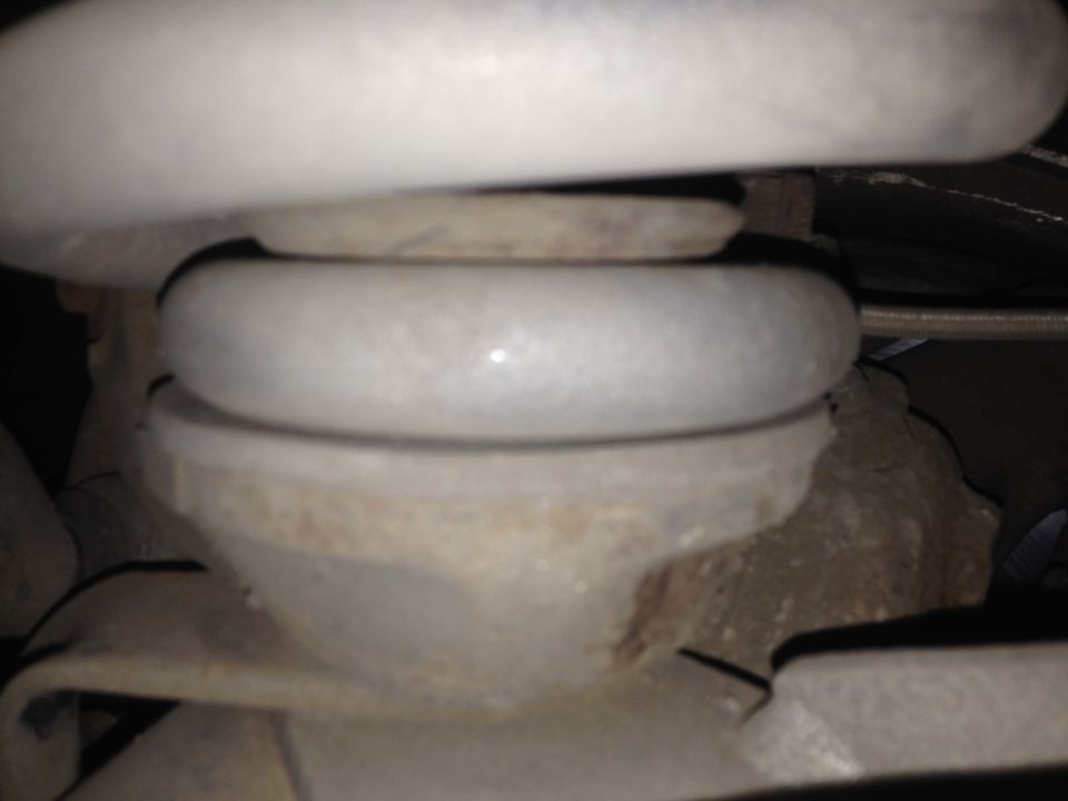 Close-up of a white vehicle coil spring on a metal mount.