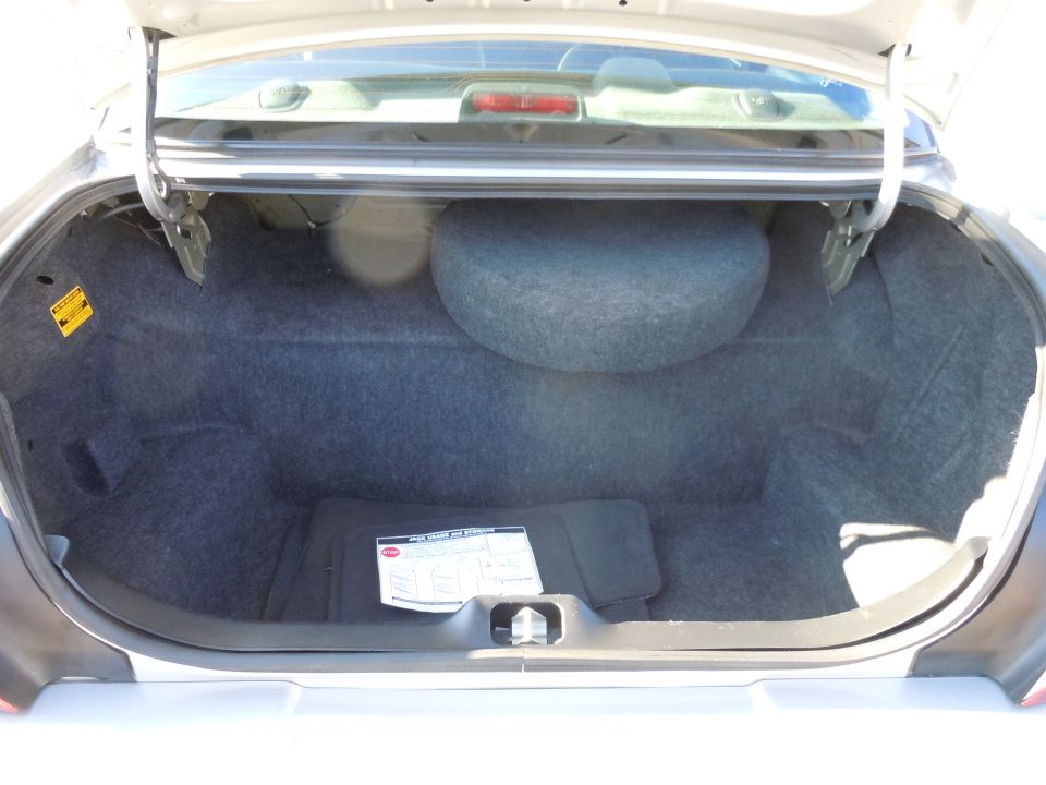 Open trunk of a sedan showing carpeted interior, spare tire, and a yellow warning sticker.