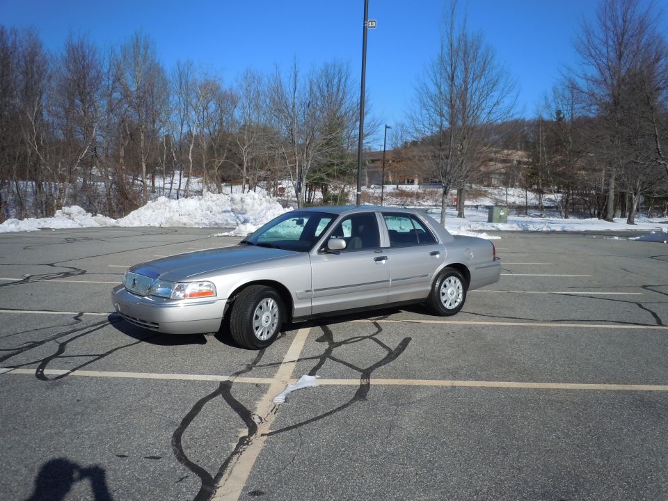 Silver 2001 Ford Crown Victoria sedan parked in a lot with snow and trees.